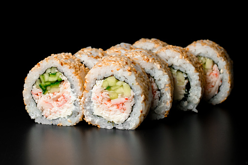 tasty sushi rolls california with snow crab meat, cream cheese, cucumber garnished sesame seeds on dark background.