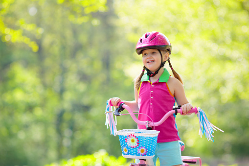 Child riding bike. Kid on bicycle in sunny park. Little girl enjoying bike ride on her way to school on warm summer day. Preschooler learning to balance on bicycle in safe helmet. Sport for kids.