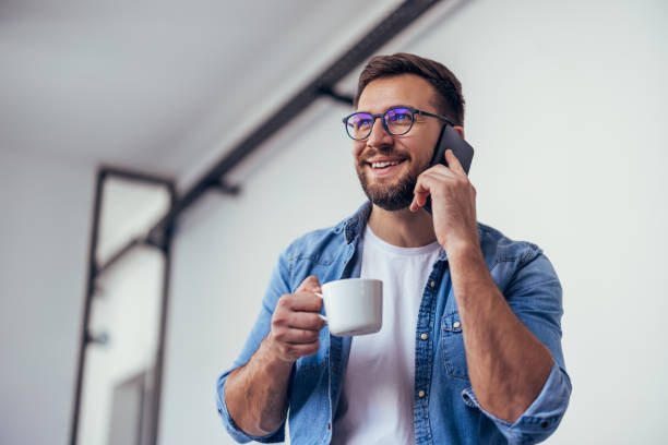 istock Handsome bearded man leaning on office desk, drinking coffee and talking on the phone. 1460313810