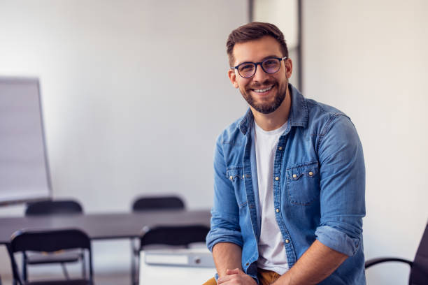 Young confident entrepreneur sitting in modern office smiling and looking at camera. stock photo