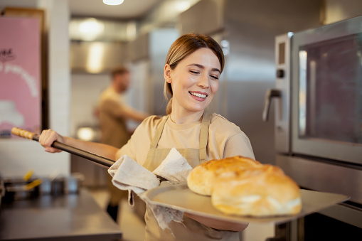 Female baker baking fresh bread in bakery shop