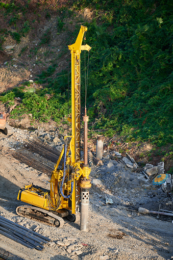 The yellow pile driver drives the foundation piles at the construction site.
