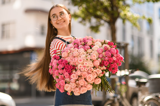 Great view on beautiful lush bouquet of fresh roses of different pink colours which happy smiling woman holds