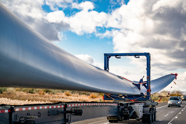 istock Big rig semi truck with an additional frame and trolley transports oversize load a super long blade of a wind turbine with an escort car 1460319926