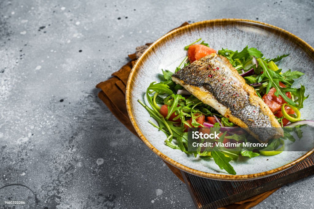 Fried sea bass fillet with vegetable salad, Dicentrarchus fish. Gray background. Top view. Copy space Fried sea bass fillet with vegetable salad, Dicentrarchus fish. Gray background. Top view. Copy space. Sea Bream Stock Photo
