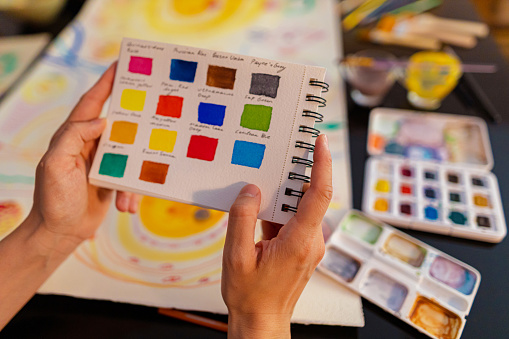 A close-up view of a color palette catalog a female artist holding and choosing for her painting.