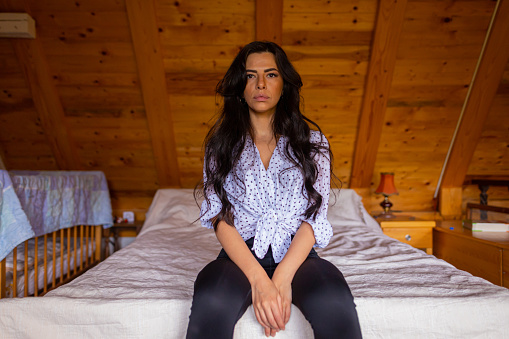 Portrait view of young white woman with long dark hair sitting in the bedroom