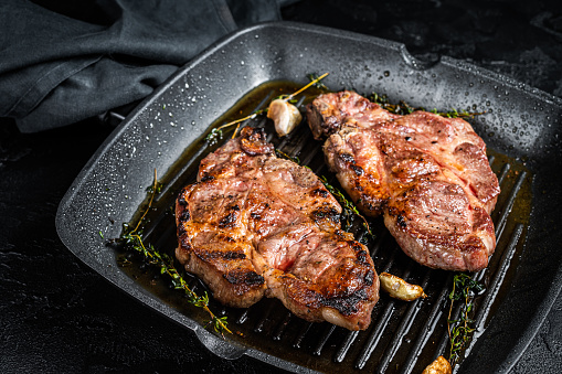 Grilled Pork steaks, neck meat on grill pan. Black background. Top view.