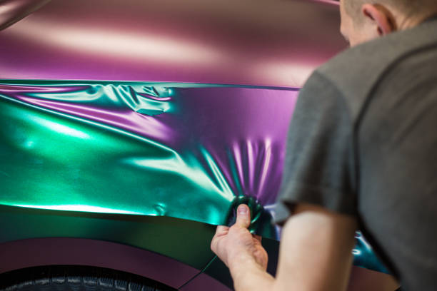 uno specialista nell'avvolgere un'auto con film in vinile color camaleonte nel processo di lavoro. gli specialisti del car wrapping coprono l'auto con fogli o pellicole in vinile. - shawl foto e immagini stock