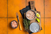 Tin with Canned tuna fillet meat in olive. Orange background. Top view