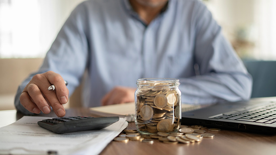 Close-up Adult man using calculator at home. coin jar on the table