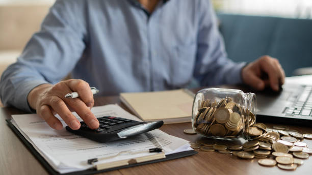 istock Close-up Man using overturned coin jar and calculator 1460330163
