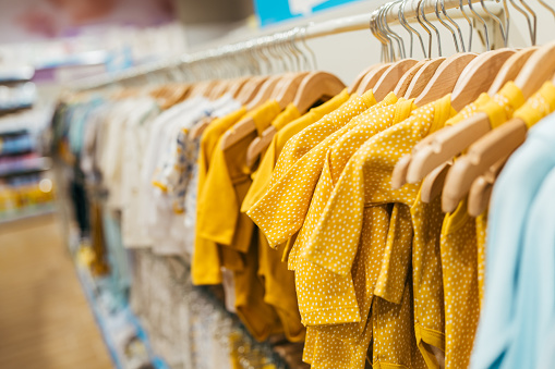 Beautiful baby clothes hanging arranged on rack in a modern store or shop. Shopping interior  concept. No people.