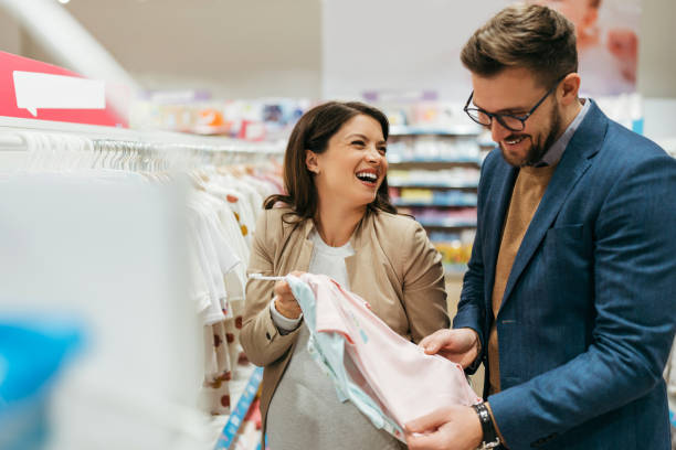 Young couple in baby shop Attractive middle age couple enjoying in buying clothes and appliances for their new baby. Heterosexual couple in baby shop or store. Expecting baby concept. baby boutique stock pictures, royalty-free photos & images