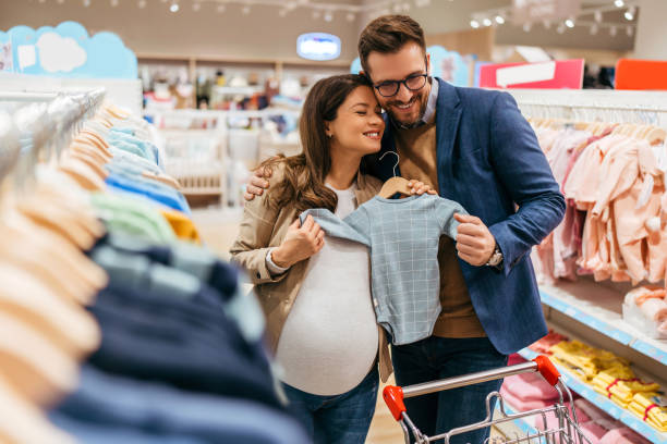 Young couple in baby shop Attractive middle age couple enjoying in buying clothes and appliances for their new baby. Heterosexual couple in baby shop or store. Expecting baby concept. baby boutique stock pictures, royalty-free photos & images