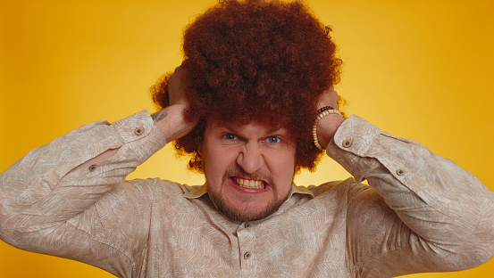 Angry man with lush Afro hairstyle coiffure screams from stress tension problems feels horror hopelessness fear surprise shock expresses gestures rage. Young depressed guy on yellow studio background