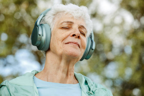 Elderly woman in headphones listens to music in the park, concepts about elderly, seniority and wellness aging stock photo