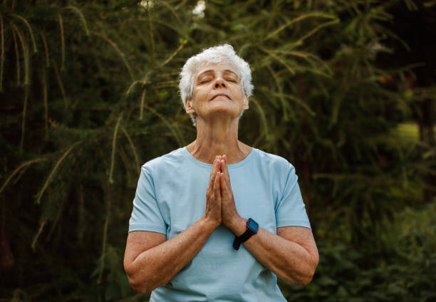 Elderly woman with short hair practicing yoga and tai chi outdoors. Old female meditating. stock photo