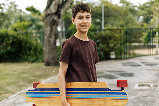 Portrait of a teenager boy holding his skateboard in the park
