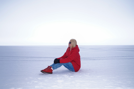 A young woman is blonde in a red jacket and sunglasses. Endless expanses on the Gulf of Finland. Snowy winter.