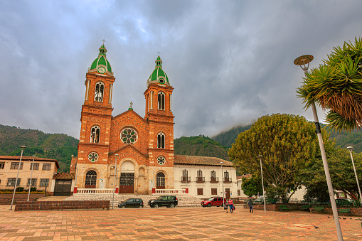 Sesquilé Colombia - August 14, 2021: The Roman Catholic church on the main square in the 400-hundred-year-old town of Sesquilé in the Department of Cundinamarca. The town was founded in 1600. It is located at an altitude of over 8,500 feet above mean sea level on the Andes Mountains. The image was shot in the morning sunlight on an overcast day. Horizontal format. Copy space.