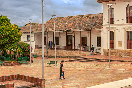 Sesquilé Colombia - August 14, 2021: Looking to one side of the main square in the 400-hundred-year-old town of Sesquilé in the Department of Cundinamarca. The town was founded in 1600. It is located at an altitude of over 8,500 feet above mean sea level on the Andes Mountains. In the centre is a local bank. The image was shot in the morning sunlight on an overcast day. Horizontal format. Copy space.