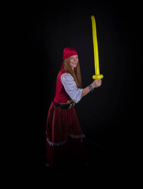 woman with long hair dressed as a pirate in a red suit and with a yellow balloon in the shape of a sword in her hand and on a black background photography of party events