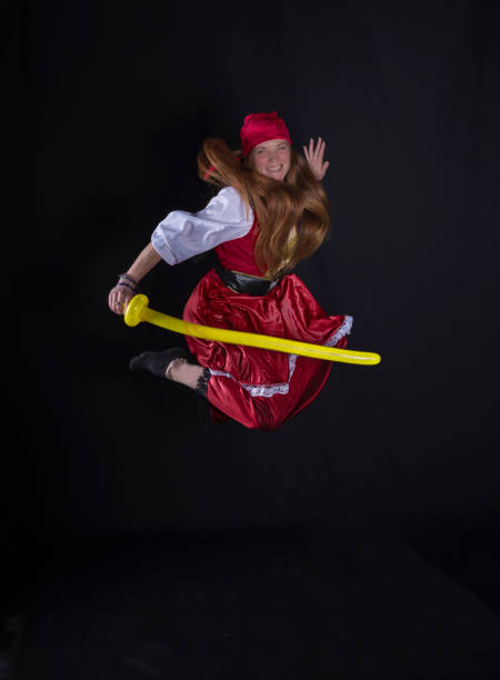 woman with long hair dressed as a pirate in a red suit and with a yellow balloon in the shape of a sword in her hand and on a black background photography of party events