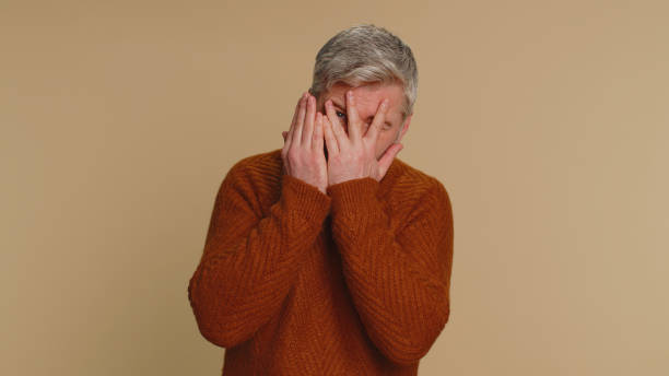 istock Curious middle-aged old man closing eyes with hand and spying through fingers, hiding and peeping 1460355140