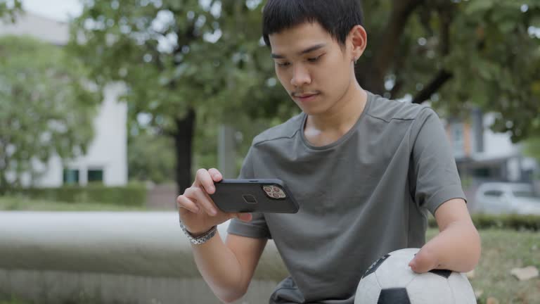 Smiling footballer holding ball and using smartphone