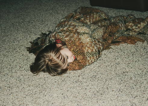 Photo adjusted to look vintage.  Little girl sleeping on the rugged floor in an earth-toned afghan blanket.