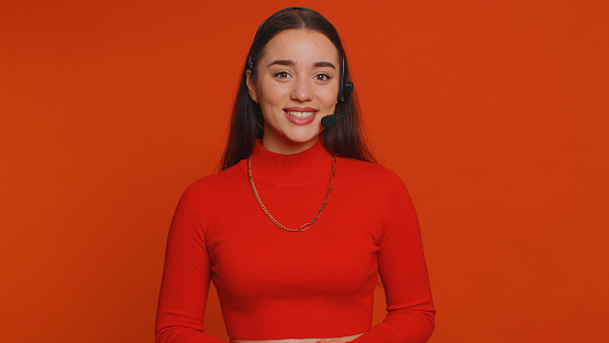 Smiling pretty woman wearing headset, freelance worker, call center or support service operator helpline, having talk with client or colleague, communication support. Young girl on red background