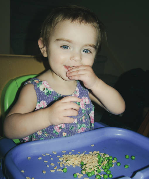 vintagae olhando foto da menina comendo ervilhas e crocantes de arroz na cadeira alta - baby goods flash - fotografias e filmes do acervo