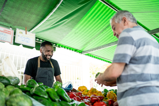 Salesman looking his customer choosing vegetables on a street market