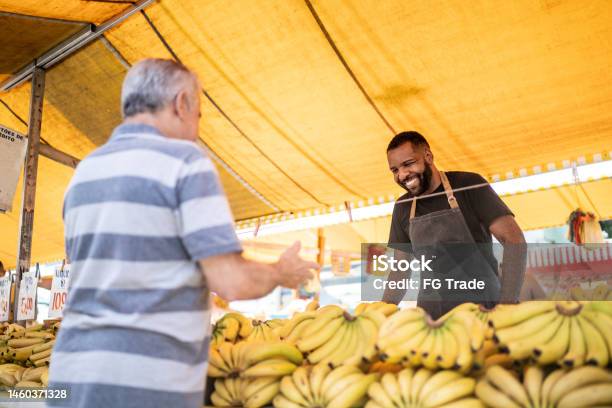 Salesman Looking To His Customer Holding A Bowl On A Street Market Stock Photo - Download Image Now