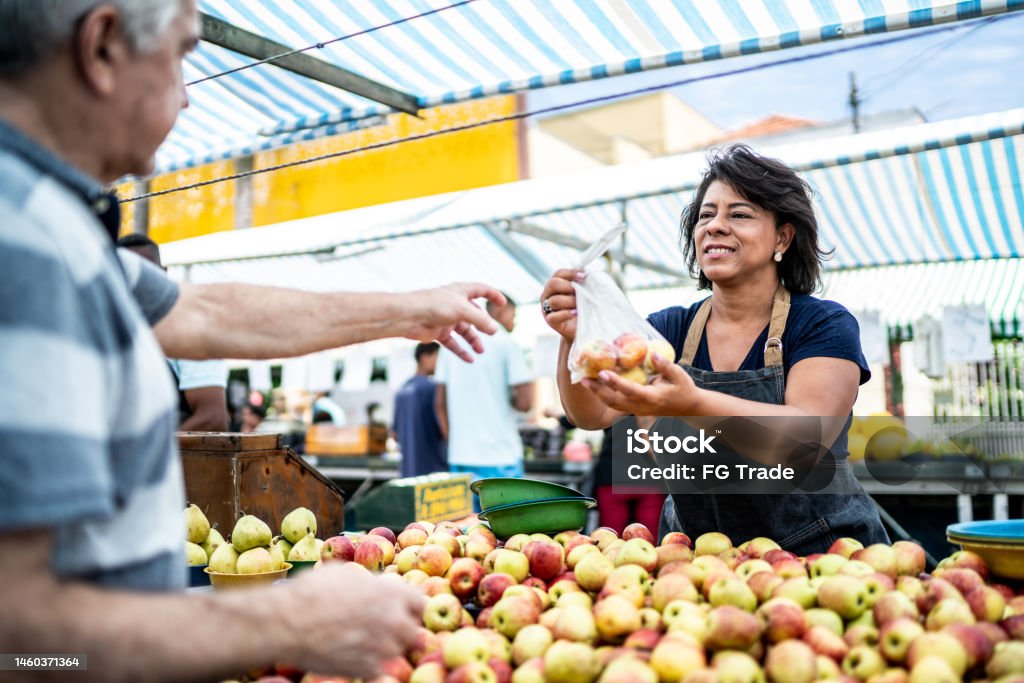 Saleswoman giving the fruits bag to her customer on a street market Market - Retail Space Stock Photo