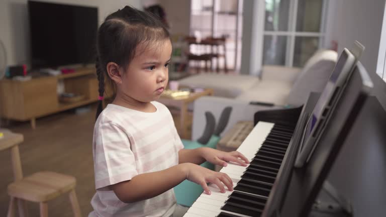 Asian little girl practicing and playing piano at home watching tutorials on a digital tablet. Online studying for musical instrument