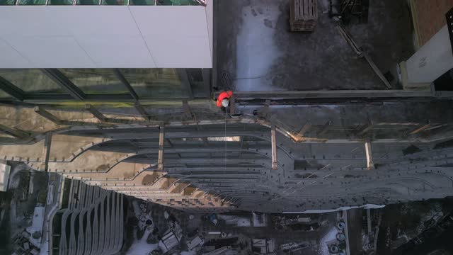 Aerial top down view of industrial climber in orange uniform drops a rope from a roof of modern high building
