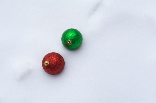 Red and green Christmas ornaments in snow during winter storm