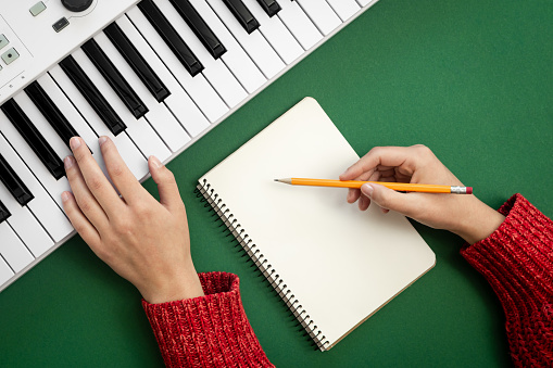 Female hands, empty notepad and music keys on green background, top view, musical creativity concept.