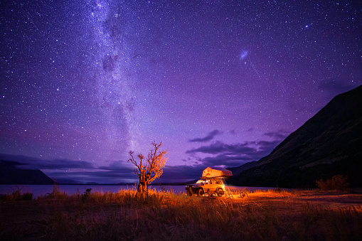 A camper van illuminated from inside standing near a beach at starry night without moon at night.