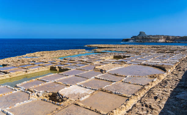 Salt pans on the coast of Gozo, Malta with Xwejni Rock in the background and blue sky stock photo