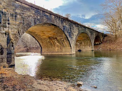 Great Cacapon, West Virginia, USA - January 26, 2023: View of a historic stone railroad bridge crossing the Cacapon River near where it flows into the Potomac River and used by CSX Transportation freight railroad and Amtrak passenger trains.