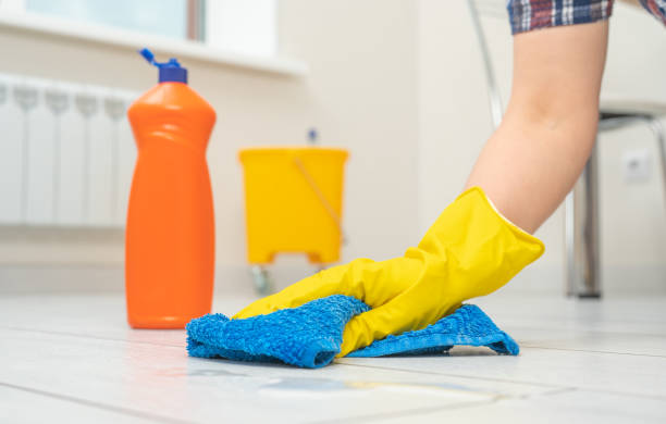 床を掃除する手袋をはめた女性。ラミネートおよびフローリング用のクリーニングおよびケア製品。黄色い手袋をはめた女性の手が青いマイクロファイバークロスで木の床を拭く - 徹底的に洗う ストックフォトと画像