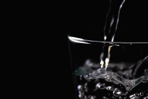 Water is pouring into a transparent glass with black background to encourage drink or saving water. World water day
