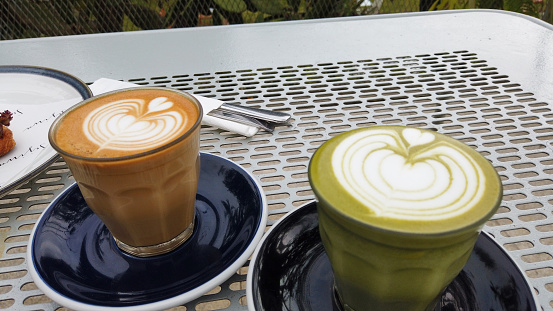 A cup of cappuccino and green tea latte on the perforated metal table