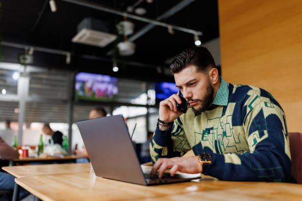 istock Handsome young man talking on mobile phone while working remotely from coffee shop 1460410535