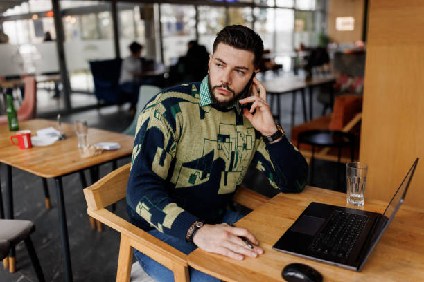 istock Young man talking on the phone while checking his email on laptop at cafe 1460410605