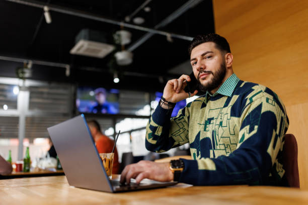 istock Handsome young man talking on mobile phone while working remotely from coffee shop 1460410721