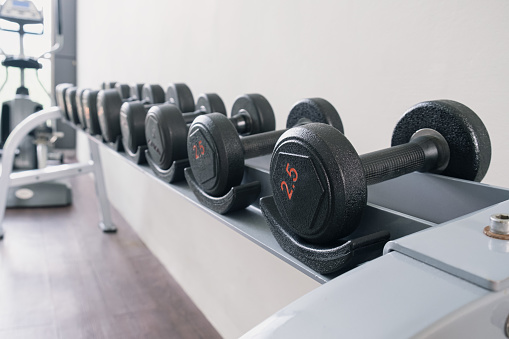 Black metal dumbbells of different weights on a rack in a gym. Sports equipment for increasing muscle mass. The concept of doing sports.